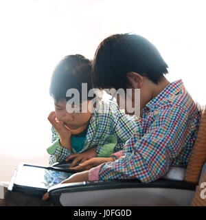 Square portrait of two young boys playing on an ipad together during a flight. Stock Photo