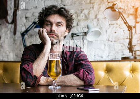 Sad and depressed guy having a beer in a pub sitting alone at a table