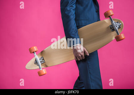 partial view of man in suit holding skateboard in hands on pink Stock Photo