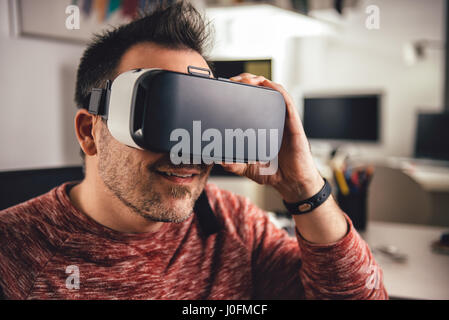 Man wearing red shirt sitting at office and using virtual reality glasses Stock Photo