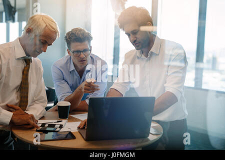 Business people talking while standing by table in office. Businessman giving demonstrating on laptop to colleagues