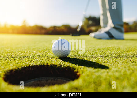 Professional golfer putting ball into the hole. Golf ball by the edge of hole with player in background on a sunny day. Stock Photo