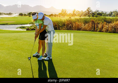 Male golf instructor teaching female golf player, personal trainer giving lesson on golf course. Male showing woman to play golf. Stock Photo