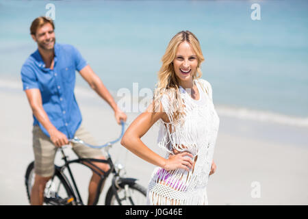 Happy woman by man riding bicycle at beach on sunny day Stock Photo