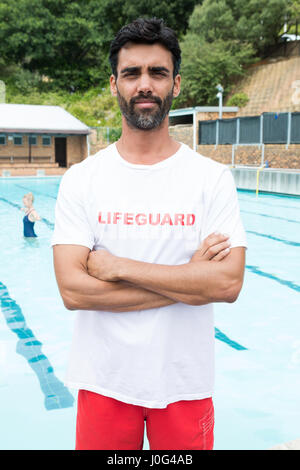 Portrait of confident lifeguard standing with arms crossed in poolside Stock Photo