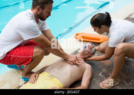 Lifeguards pressing chest of unconscious senior man at poolside Stock Photo