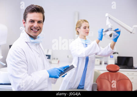 Dentist using digital tablet while his colleague adjusting dental light in background at clinic Stock Photo