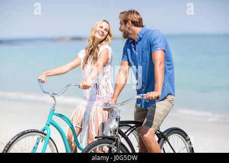 Happy couple riding bicycles at beach on sunny day Stock Photo