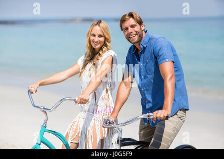 Portrait of smiling couple riding bicycles at beach on sunny day Stock Photo