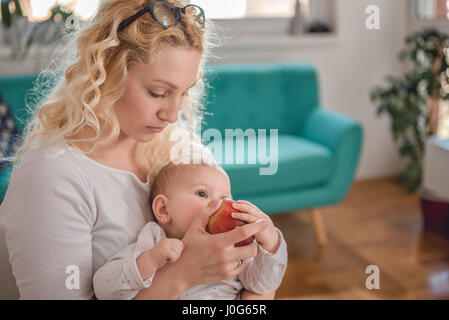 Mother feeding baby at home office with fresh red apple Stock Photo