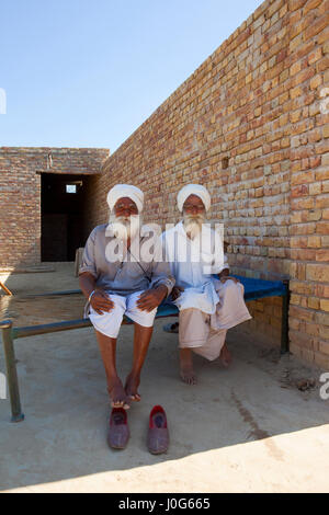 two traditionally dressed rajasthan farmers sitting on a bed at home under a clear blue sky in india Stock Photo