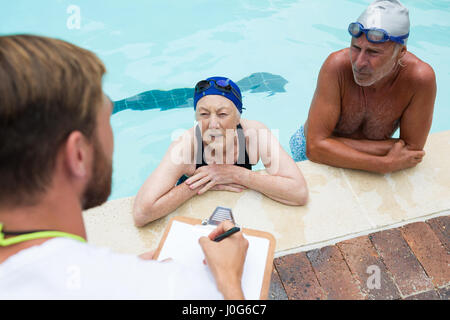 Swim coach interacting with senior couple at poolside Stock Photo