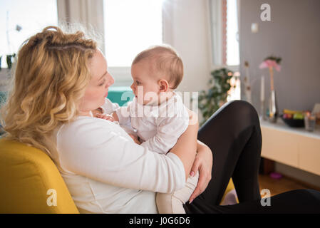 Mother holding baby in her arms and sitting at yellow armchair