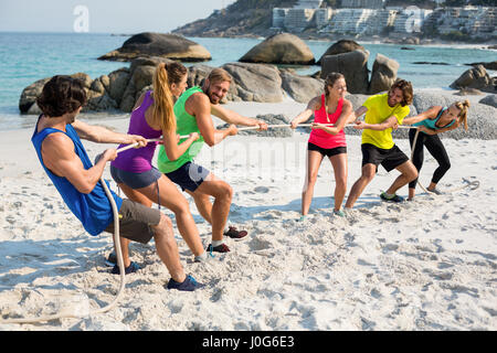 Full length of friends playing tug of war on shore at beach Stock Photo