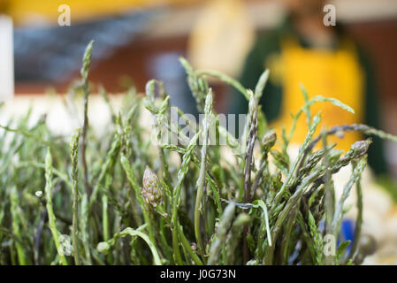 Green wild asparagus tip heads bunch on market stall, people out of focus in background Stock Photo