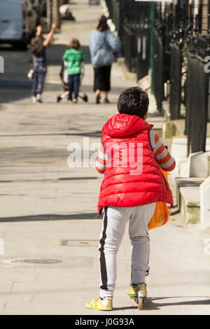 A young boy riding a scooter chases after his mother and brother and sisters on a London street Stock Photo