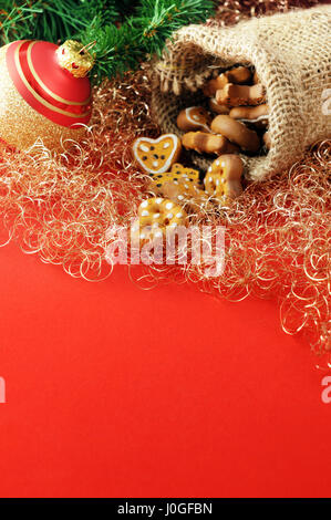 Christmas decoration like pine twig, Christmas ornament and jute bag with prezel and cookies on red copy space Stock Photo