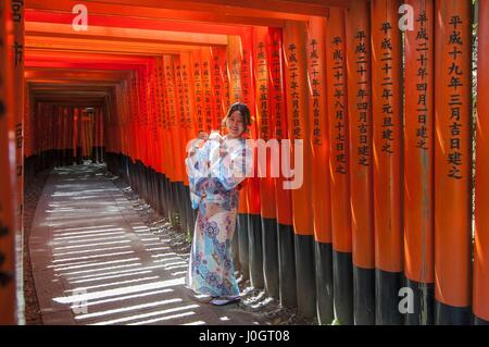 Woman dressed in traditional japanese costume walking under tori gates at the fushimi-inari shrine, Kyoto Japan Stock Photo