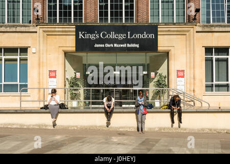 Students using mobile phones sitting outside the entrance to the James Clerk Maxwell Building, King's College London, Waterloo, Lambeth, England, U.K. Stock Photo