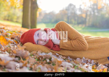 Pensive blonde woman lying in park in autumn Stock Photo