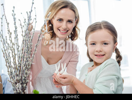 Beautiful mother and daughter holding decorative easter bunnies and smiling at camera Stock Photo