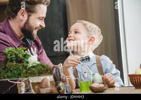 Father and son preparing for Easter painting eggs and looking at each other Stock Photo