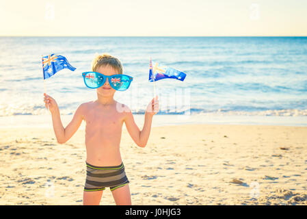 Cute smiling boy standing on the beach and holding Australian flags on Australia day Stock Photo