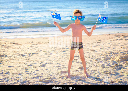 Cute smiling boy standing on the beach and holding Australian flags on Australia day Stock Photo