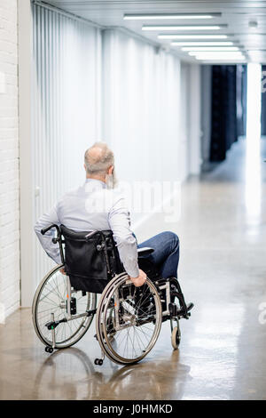 Back view of bearded senior man in wheelchair at hospital hallway Stock Photo