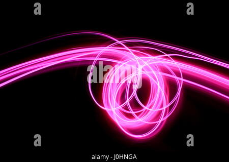 Pink light painting photography - long exposure photo of vibrant pink loops and swirls on black background.  Abstract light pattern.