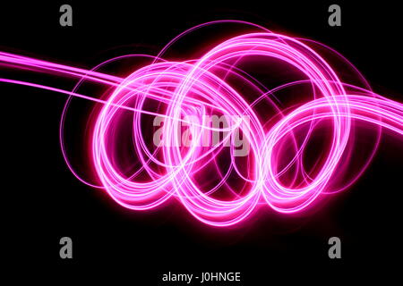 Pink light painting photography - long exposure photo of vibrant pink loops and swirls on black background.  Abstract light pattern.