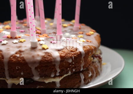 Birthday victoria sponge cake with runny icing, and pink candles, with sugar star decorations, against a black background Stock Photo