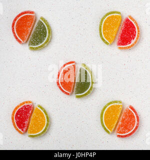 Colored sweets from marmalade in the form of slices of citrus fruits are spread out on the gray table tops in pairs. Only five pairs Stock Photo