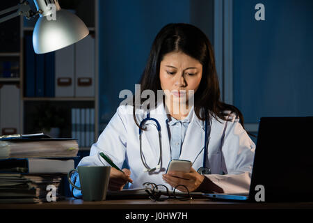 tired young female doctor received bad news from smartphone message at late night. pretty mixed race asian chinese woman model. medical and health con Stock Photo