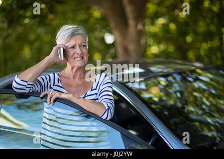 Annoyed senior woman talking on phone by car Stock Photo