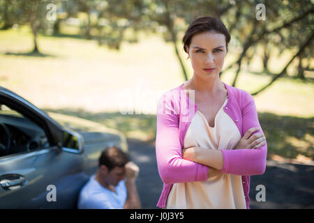Portrait of angry woman standing with man sitting by breakdown car Stock Photo