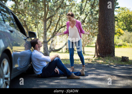 Frustrated woman shouting on man sitting by breakdown car Stock Photo