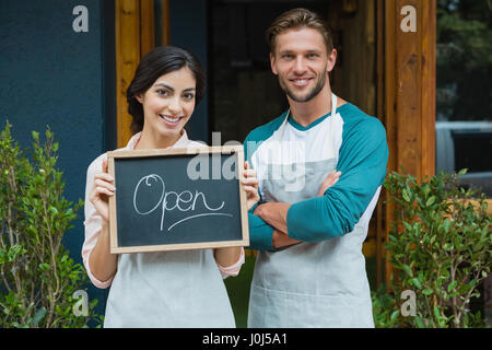 Portrait of smiling waiter and waitress standing with chalkboard outside the cafe Stock Photo