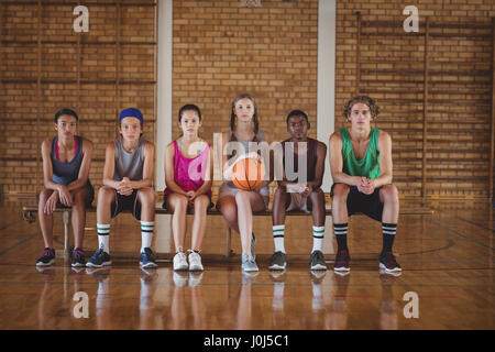 Portrait of high school kids sitting on a bench in basketball court Stock Photo