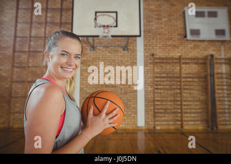 Happy high school girl standing with basketball in the court Stock Photo
