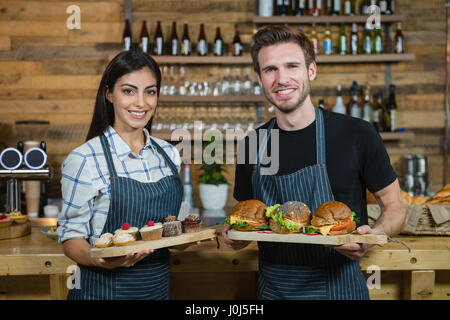 Portrait of waiter and waitresses holding cupcakes and food at counter in cafÃƒÂ© Stock Photo