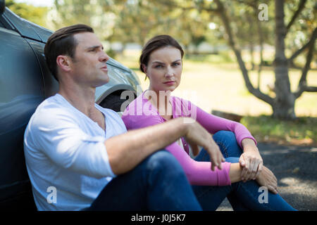 Tired couple sitting by breakdown car on road Stock Photo