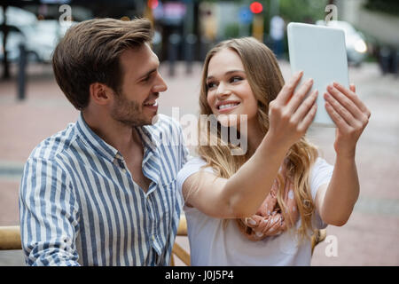 Couple holding digital tablet while sitting at sidewalk cafe in city Stock Photo