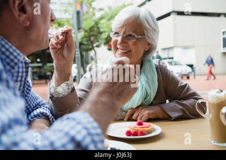 Senior woman feeding sweet food to man in outdoor cafÃƒÂ©