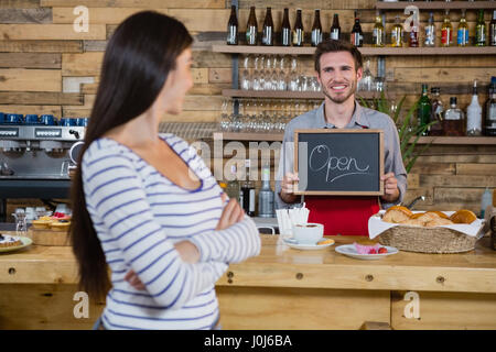 Woman standing with arms crossed while waiter holding open signboard in cafÃƒÂ© Stock Photo