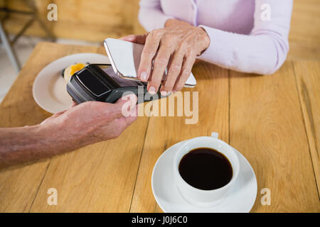 Senior woman making payment through NFC technology on mobile phone in cafÃƒÂ© Stock Photo