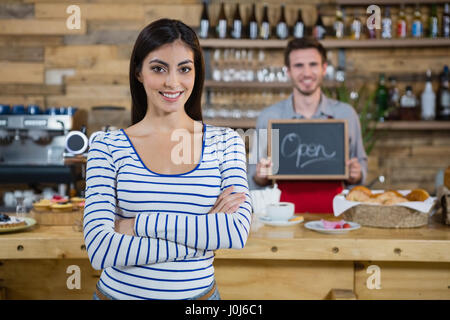 Woman standing with arms crossed while waiter holding open signboard in cafÃƒÂ© Stock Photo