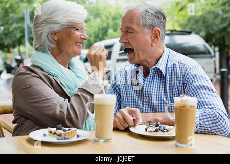 Smiling senior woman feeding tart to man in outdoor cafÃƒÂ© Stock Photo