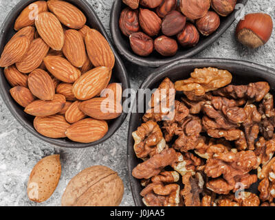 Walnuts, almonds and hazelnuts in trendy plates on gray cement background. Top view or flat lay. Stock Photo