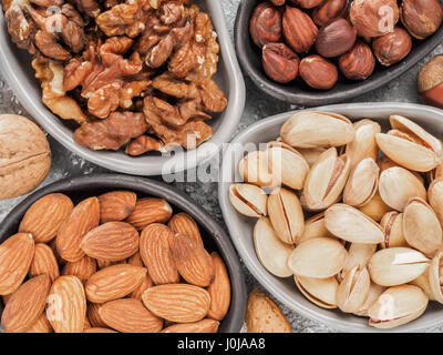 Walnuts, almonds, pistachios and hazelnuts in trendy plates on gray cement background. Top view or flat lay. Stock Photo